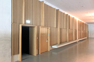  Die Flurwände der Hörsäle im ersten und zweiten Obergeschoss sind mit edlen Lamellen aus Eichenholz ausgeführt. In die vertikale Struktur sind auch die Öffnungen der INDUSILENT Überströmelemente eingebunden.  